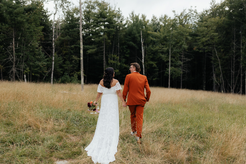 Bride and groom walking through a field at the Barn at Pinestone near Lake Placid