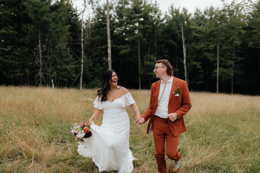 Bride and groom running through an Adirondack field 
