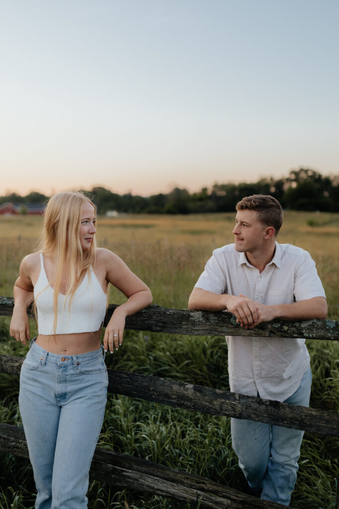 Couple in a field at sunrise leaning on a fence