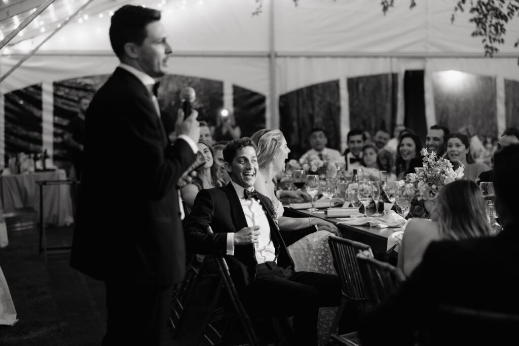 Bride and groom laugh during toast in their tented reception