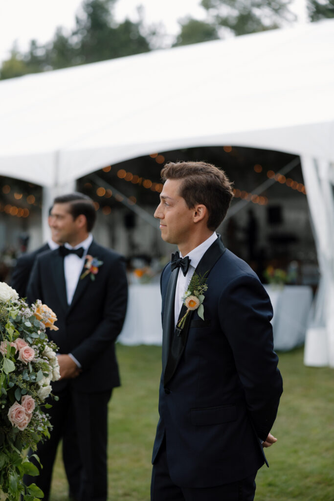 groom watches as bride arrives by boat to her lakeside ceremony in the Adirondacks