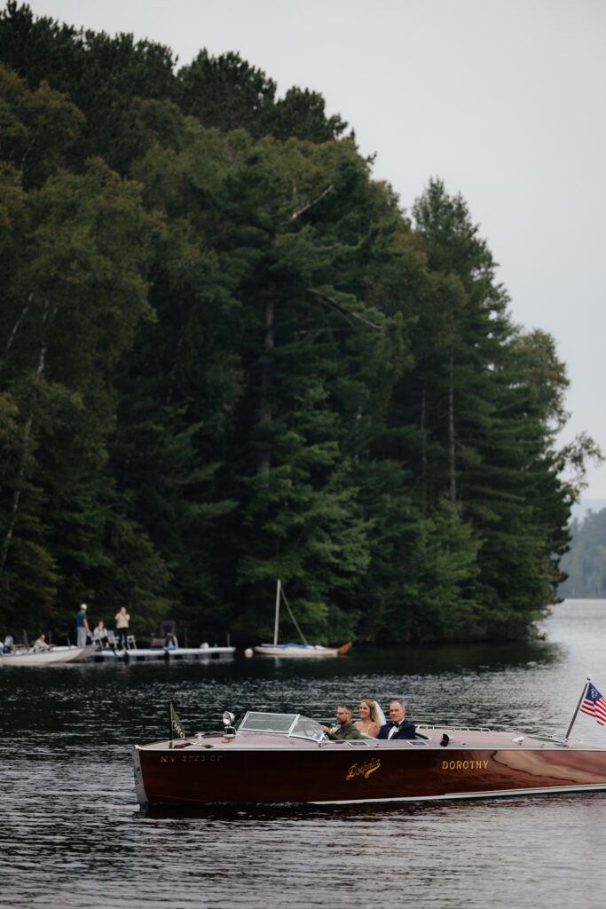 bride arrives by boat to her lakeside ceremony in the Adirondacks